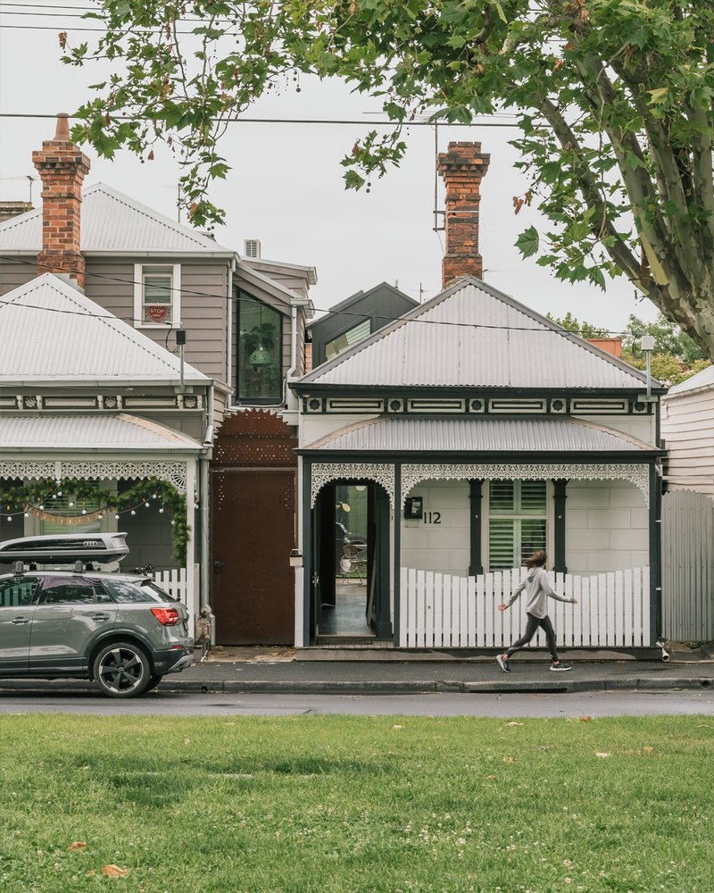 Street facade of a Victorian cottage with white corrugated roofing and a pedestrian crossing the footpath