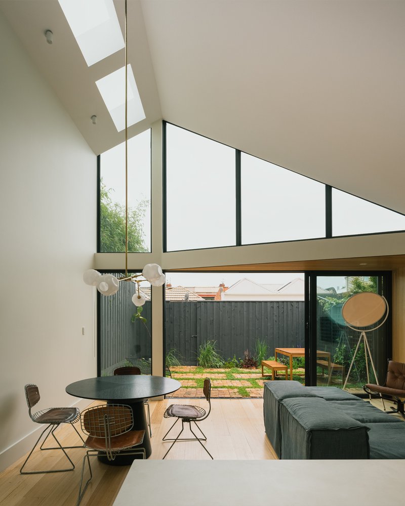 Double-height living space with angled skylights and full-height glazing opening to a courtyard with timber pavers