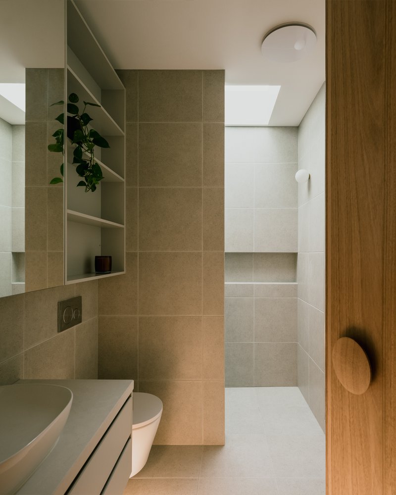 Bathroom with beige tile partition separating vanity from walk-in shower under a skylight