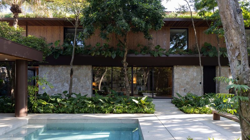 Two-storey facade with stone base and timber upper volume facing a pool deck surrounded by tropical planting