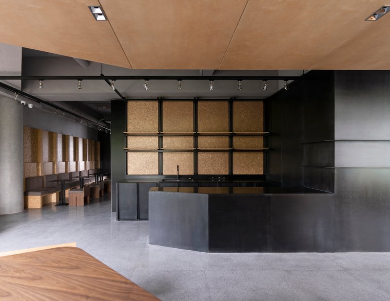Reception desk in blackened steel with cork-paneled wall grid and track lighting above