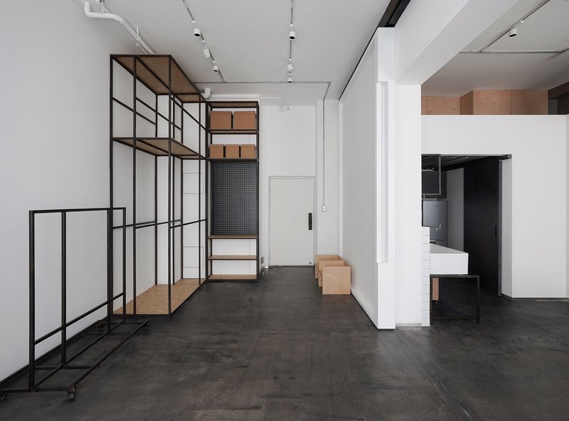 Corridor with freestanding black metal shelving unit holding timber boxes alongside white service core