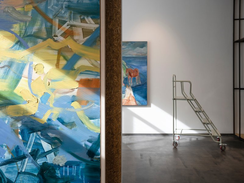 Gallery interior with abstract paintings on white walls and a metal rolling ladder on polished concrete
