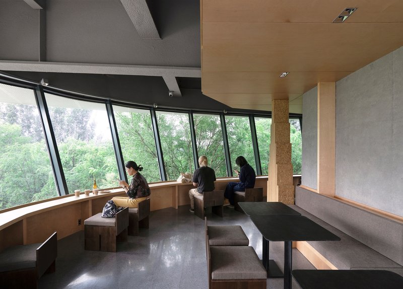Seating alcove with angled windows overlooking greenery and three visitors at built-in benches