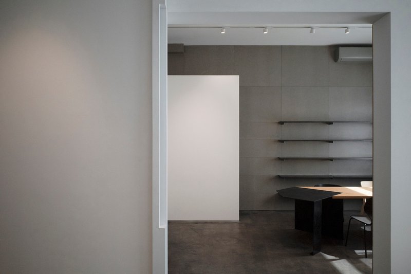 View through doorway into gallery space with floating shelves and desk illuminated by track lighting