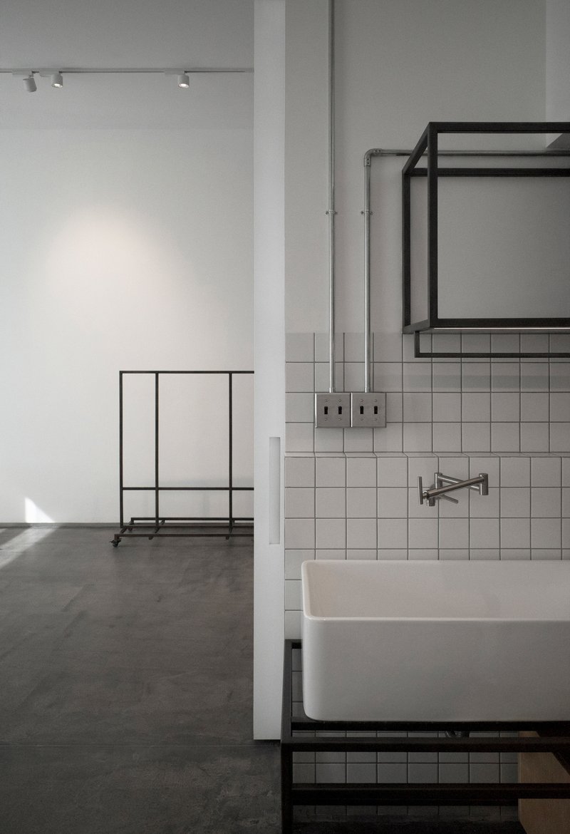 White square tile backsplash behind a basin with exposed conduit and black steel clothing rack