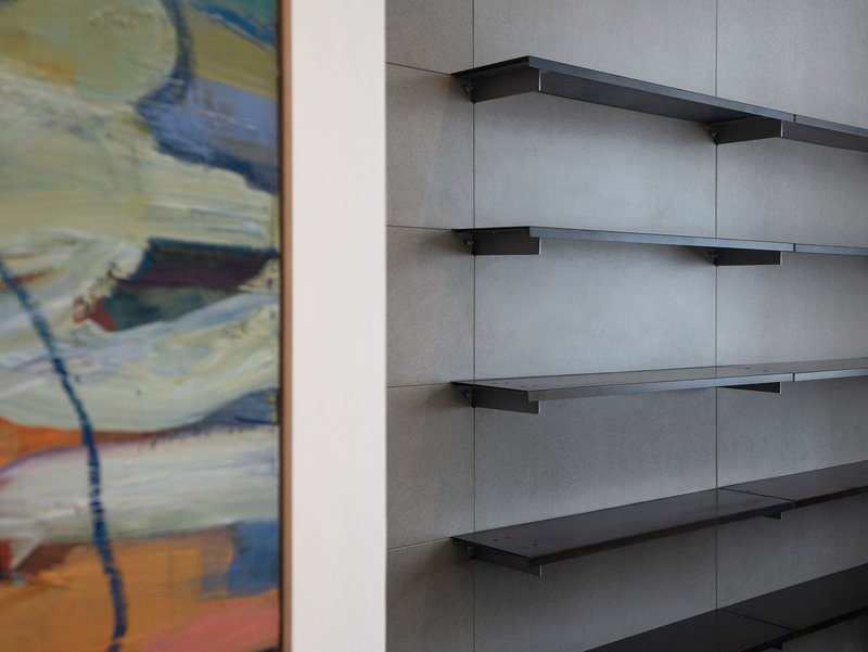 Black metal shelving brackets mounted on grey panel walls beside a framed painting