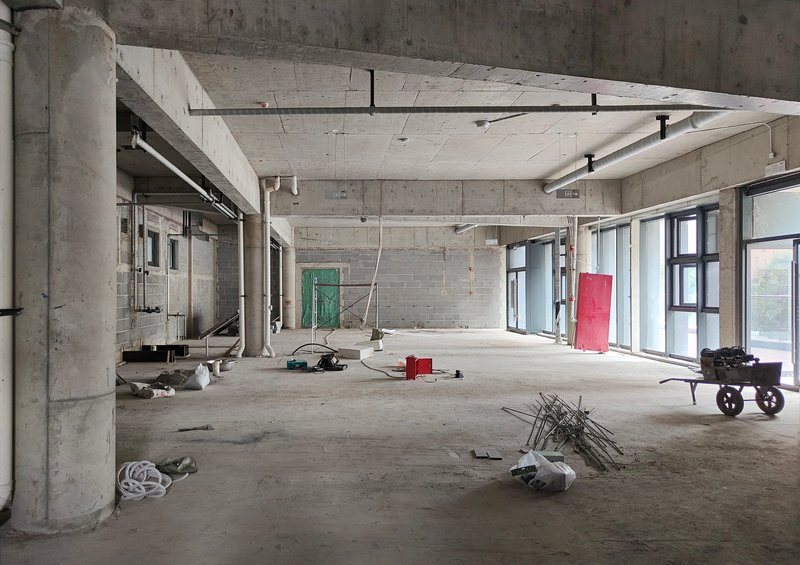 Unfinished concrete interior with exposed columns, beams, and construction materials scattered on the floor