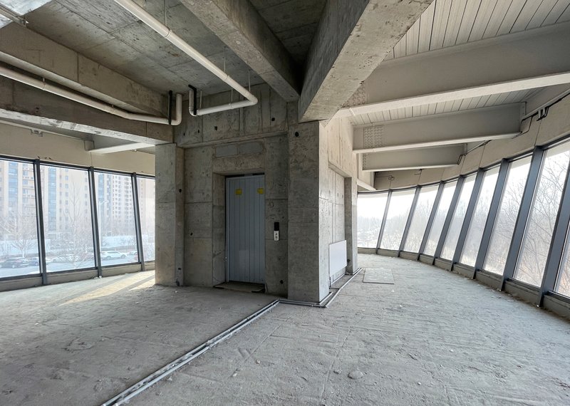 Raw concrete corner with elevator doors and angled curtain wall windows during construction