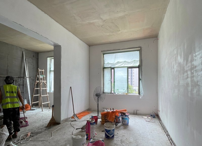 Plastered room under construction with a worker in high-visibility vest and paint buckets near the window