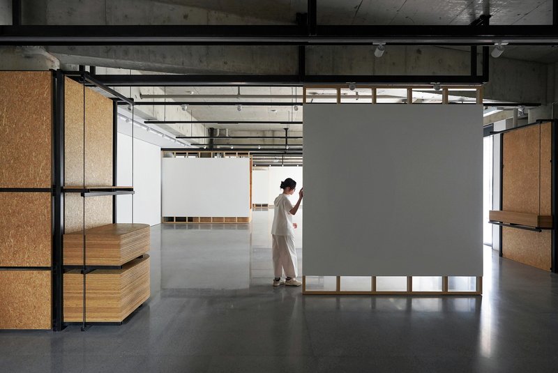 Open gallery space with black steel partitions, cork panels, and a visitor adjusting a movable wall