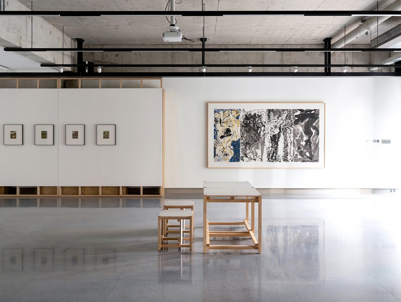Gallery room with exposed concrete ceiling, timber furniture, and framed artworks on white walls