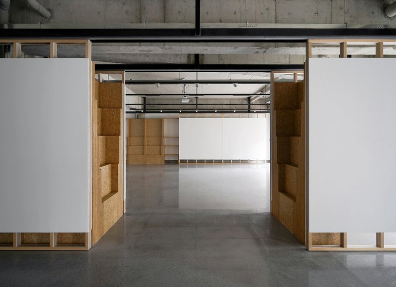 View through doorway framed by cork-paneled walls leading to connected exhibition spaces beyond