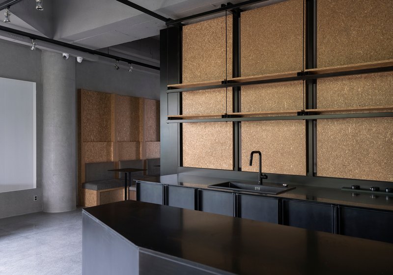 Kitchenette with black metal cabinetry and cork-paneled walls within a gallery support space