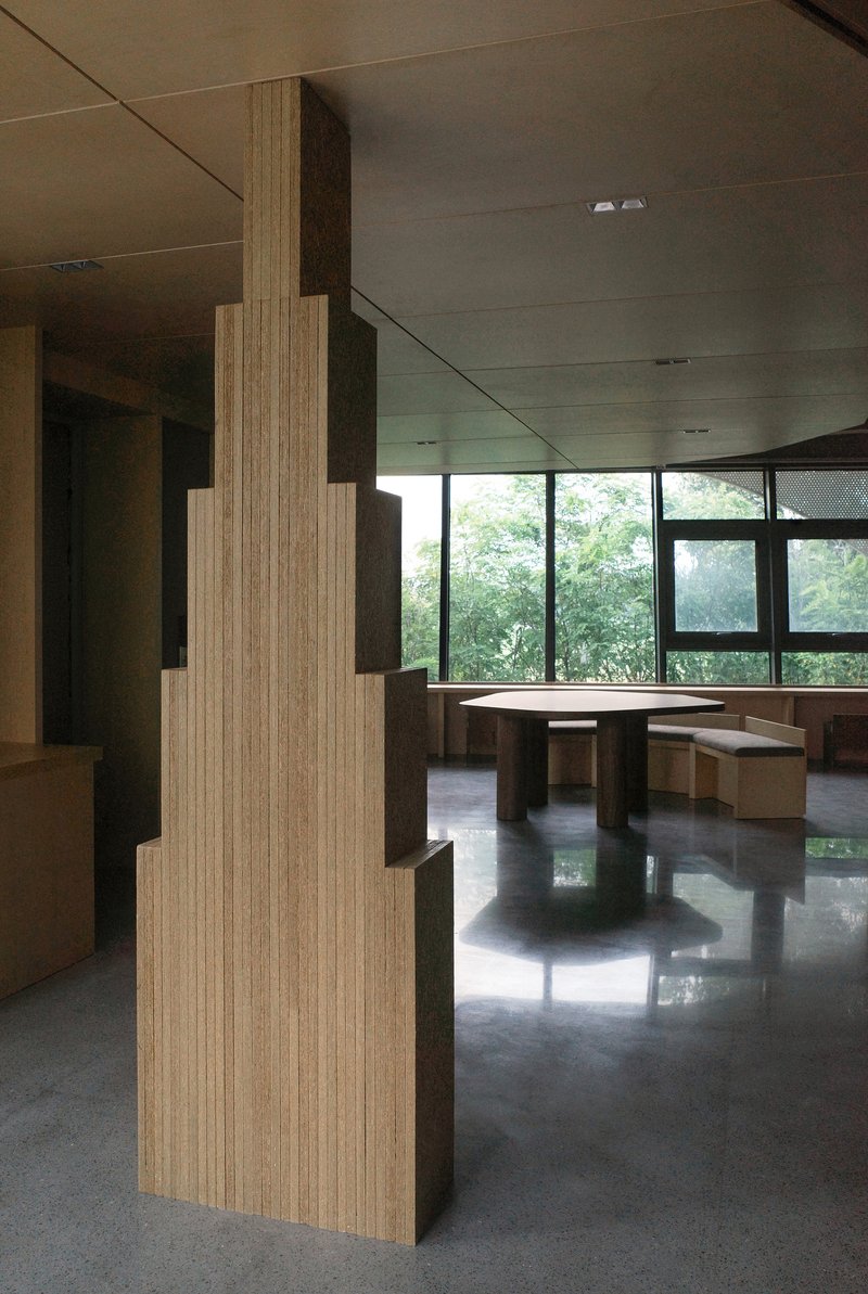 Stepped timber column with layered profile beside seating area framed by corner windows