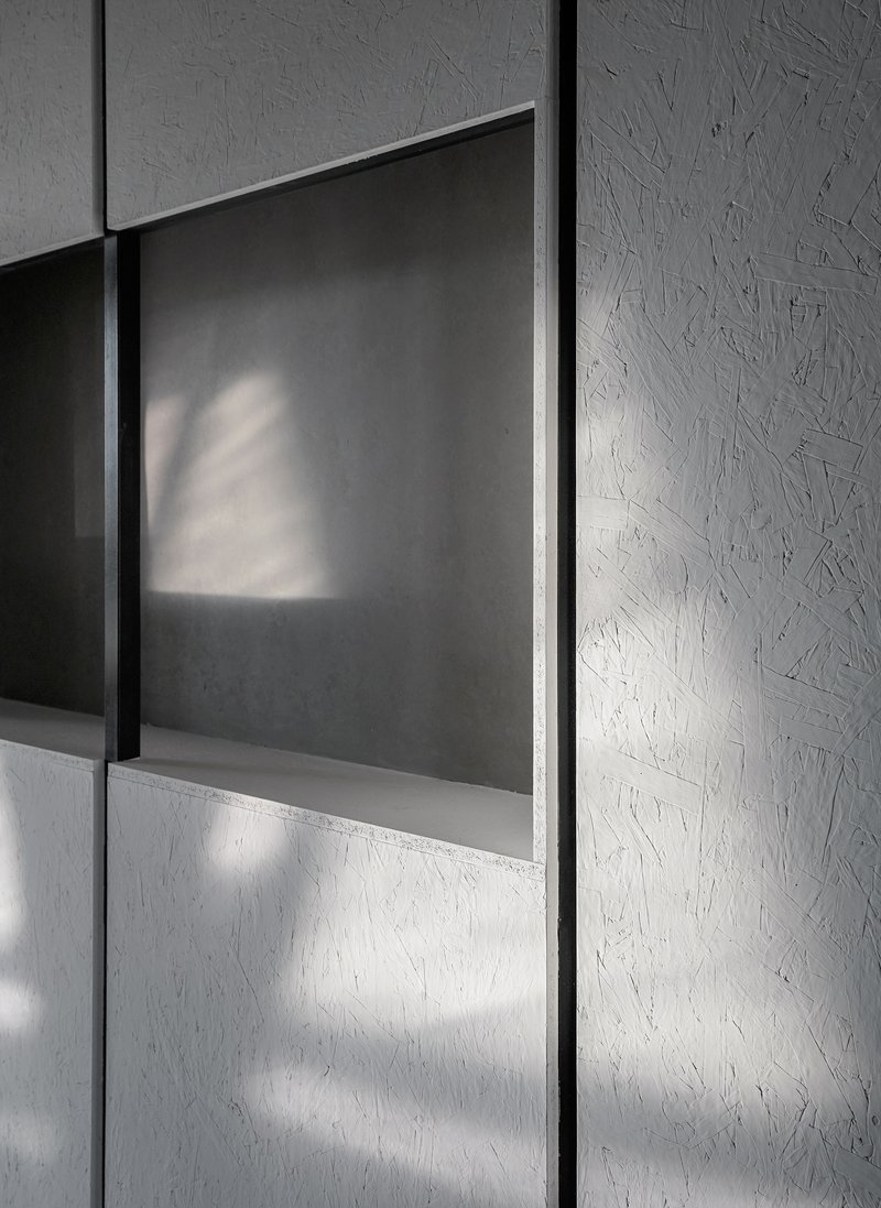 Detail of grey panel wall with recessed opening casting angular shadows in natural light