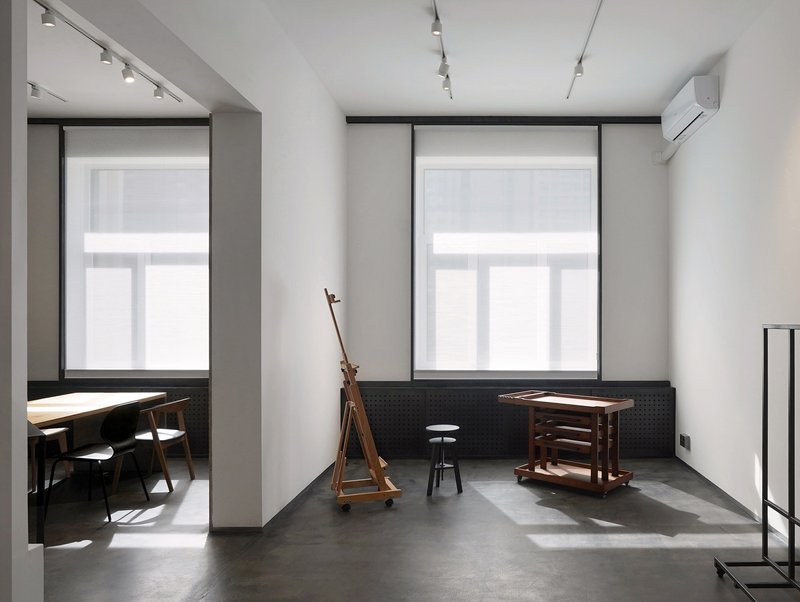 Gallery room with polished concrete floor and wooden easel beside two tall windows with roller blinds
