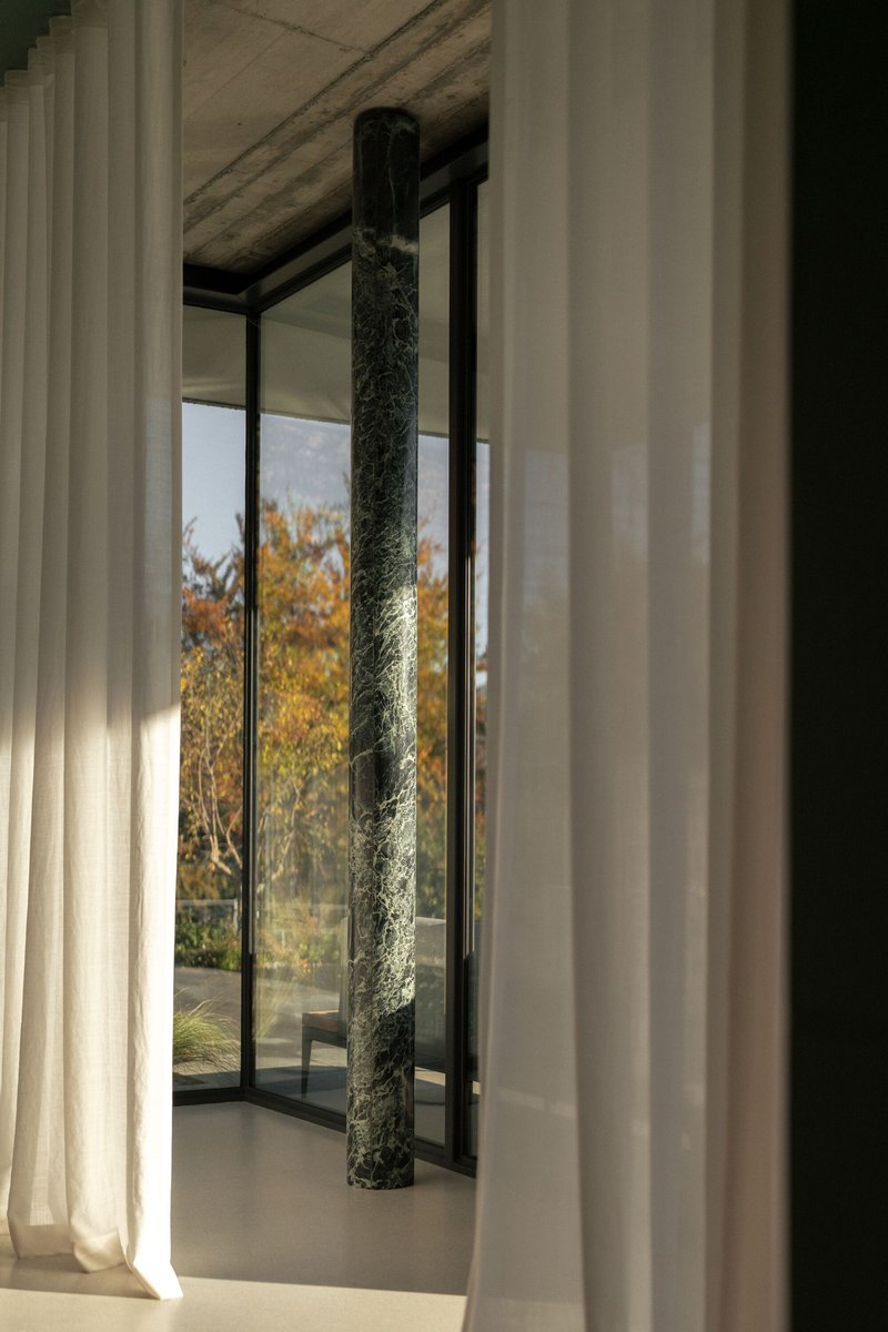 Interior view through sheer curtains to a dark marble column and glazed courtyard in autumn