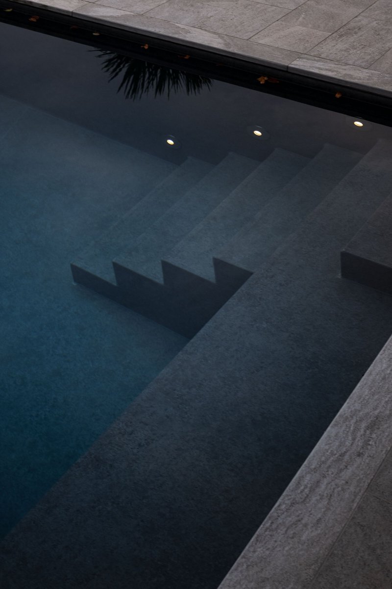 Evening view of rectangular pool with submerged steps and recessed lighting reflecting concrete edges