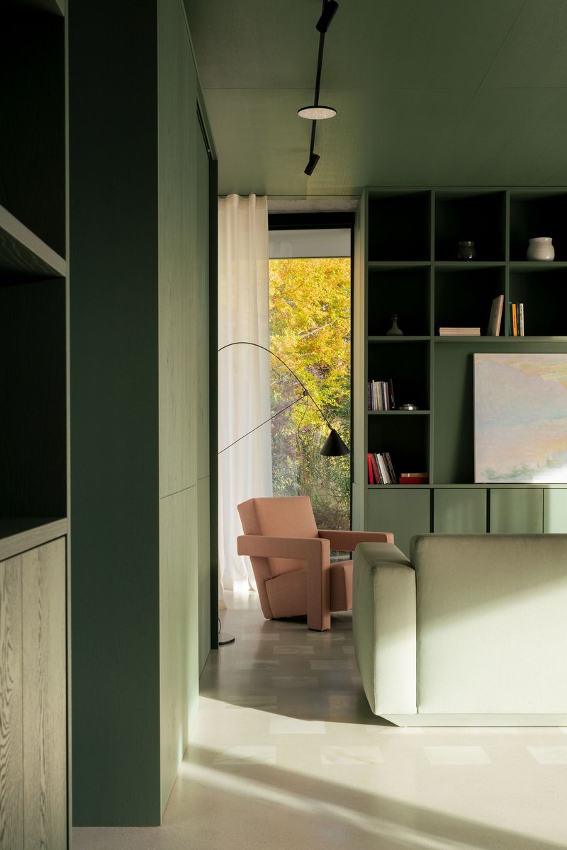View through green kitchen passage to living area with pink armchair and yellow autumn foliage visible through window