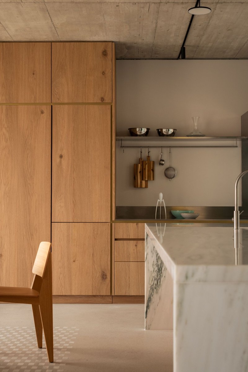 Kitchen corner with oak paneled cabinetry and marble island under exposed concrete ceiling with hanging utensils