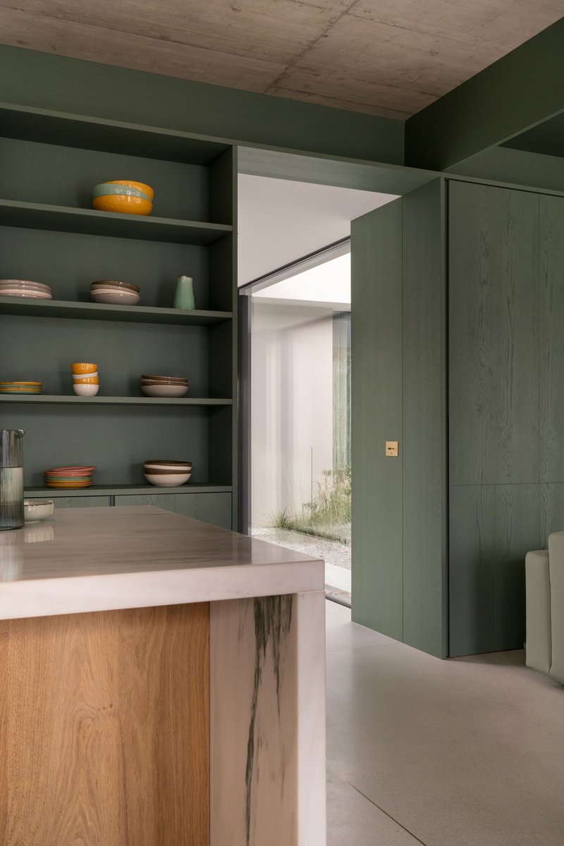 Kitchen island with green shelving displaying ceramic bowls and view through to courtyard with planted grasses