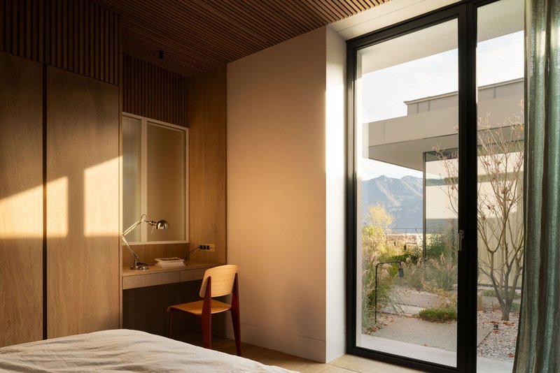 Bedroom workspace with built-in oak desk facing full-height glazing and mountain view beyond bare trees