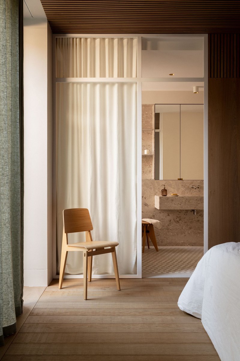 Bedroom threshold with sheer curtain dividing sleeping area from stone-clad bathroom with mosaic floor