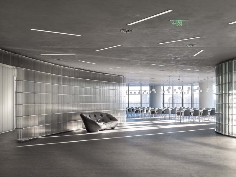 Reception lounge with translucent vertical panel walls and a dark tufted sofa beneath linear ceiling lights