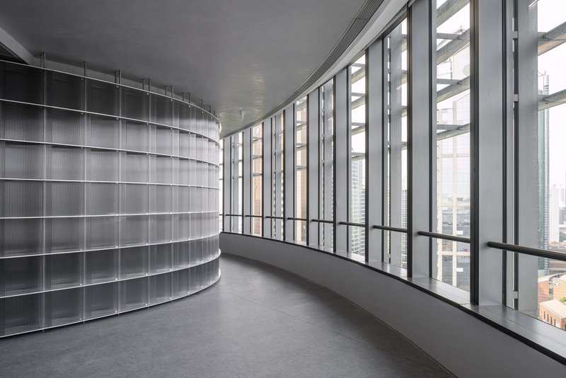 Perimeter corridor with floor-to-ceiling glazing and a curving translucent glass block interior wall