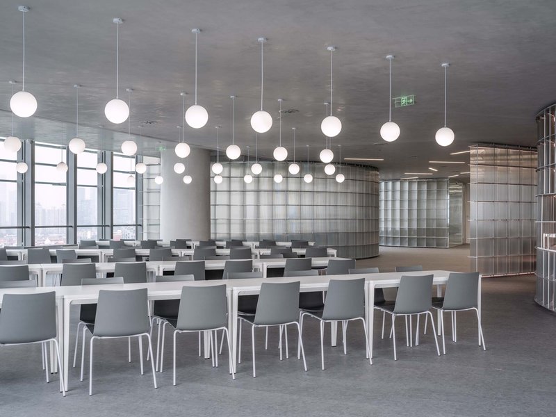 Dining hall with white tables, gray chairs, and rows of spherical pendant lights under cloudy sky