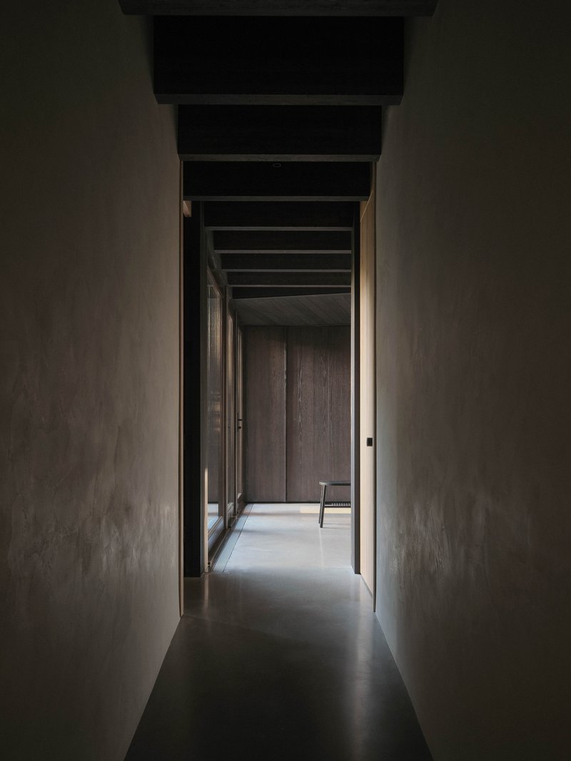 Narrow corridor with polished concrete floor and exposed ceiling beams framed by smooth plaster walls