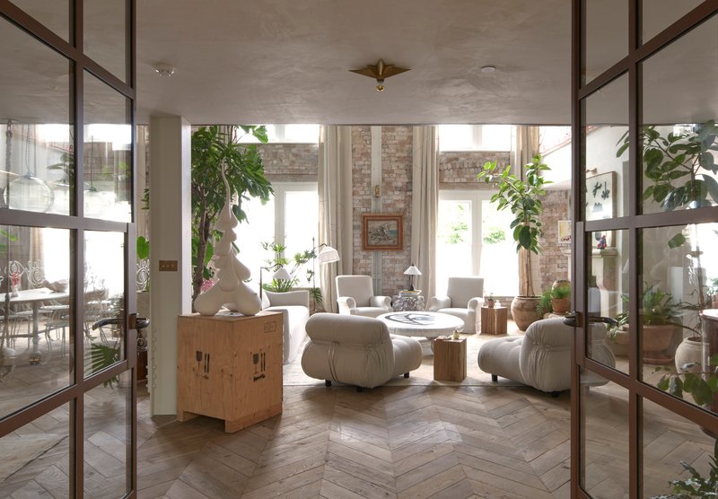 View through open steel-framed doors into a living room with exposed brick fireplace and soft natural light