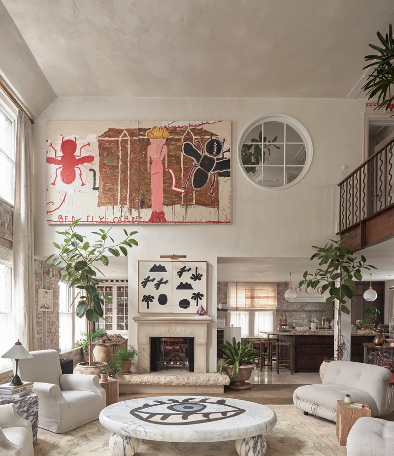 Double-height living space with exposed brick walls, round porthole window, and fireplace below graphic artwork