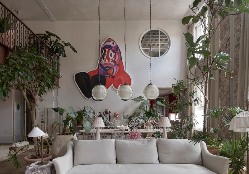 Double-height living room with circular window, suspended globe lights, and abundant potted plants beneath a decorative rocket mural
