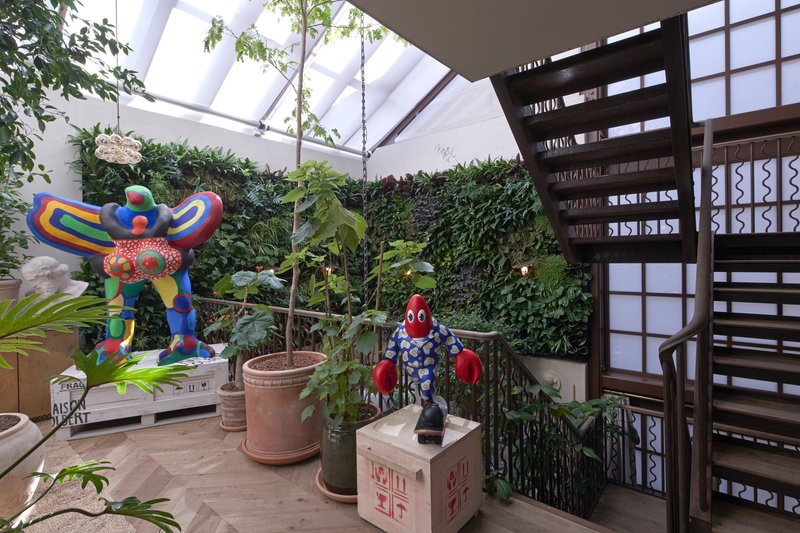 Glazed skylight atrium with vertical green wall, sculptural figures in planters, and dark timber staircase with patterned railings