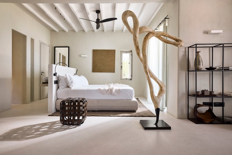 Bedroom with exposed white timber ceiling beams and driftwood sculpture illuminated by afternoon sunlight