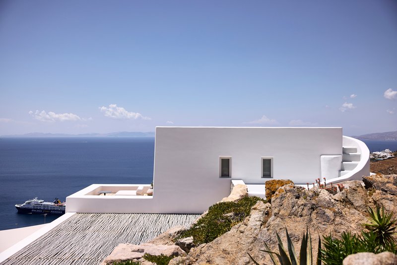 White rendered facade with curved spiral staircase and two small windows overlooking the blue sea