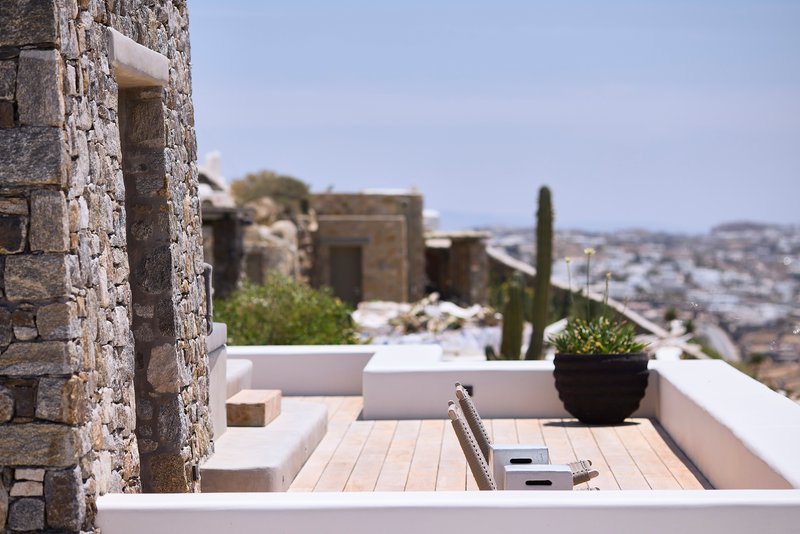 Timber deck terrace with recessed seating alongside stone wall and planted pot under bright sunlight