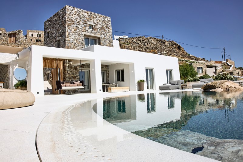 Poolside terrace with curved mosaic edge stepping into water beside white colonnade and stone tower volume