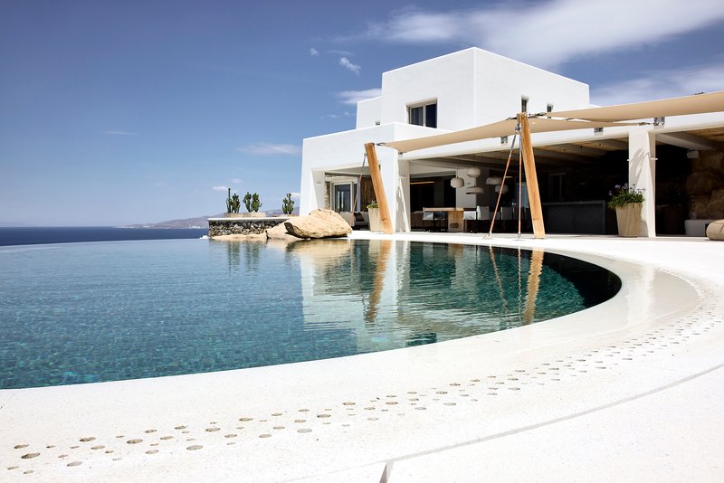 Infinity pool edge with timber pergola columns reflected in still water
