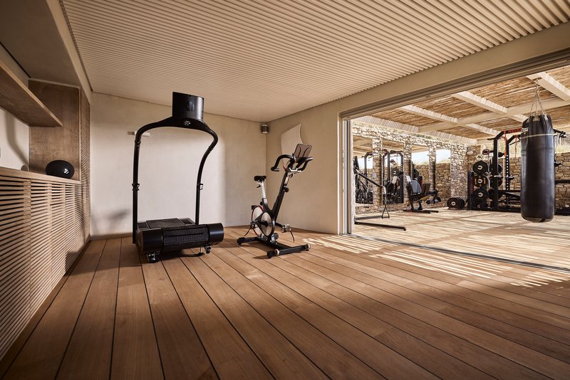 Interior fitness room with slatted timber ceiling and decking opening to an outdoor exercise area with stone walls