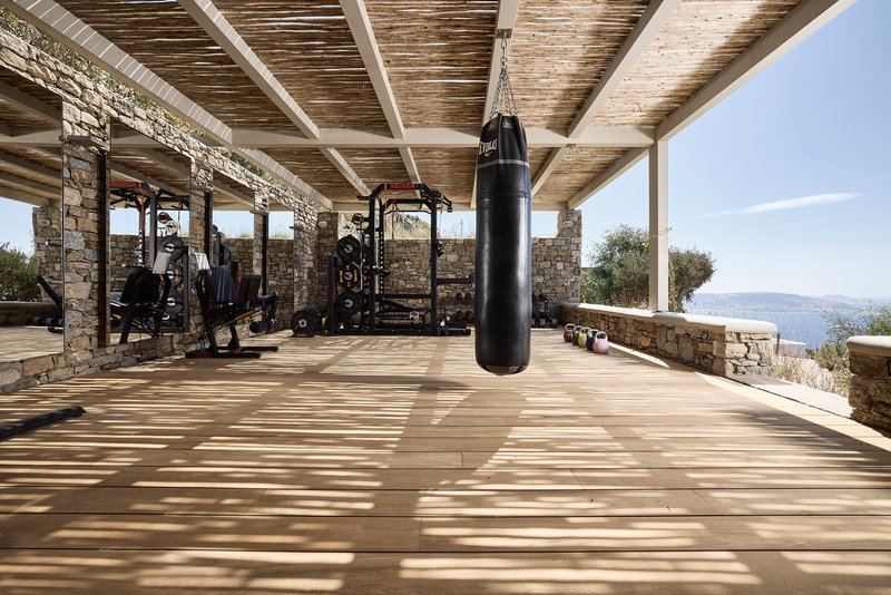 Covered outdoor gym pavilion with exposed timber beams and hanging punching bag overlooking distant hillside landscape
