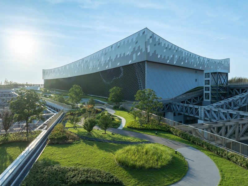 View of the curving pathway through the lawn leading toward the elevated pedestrian bridge below the building