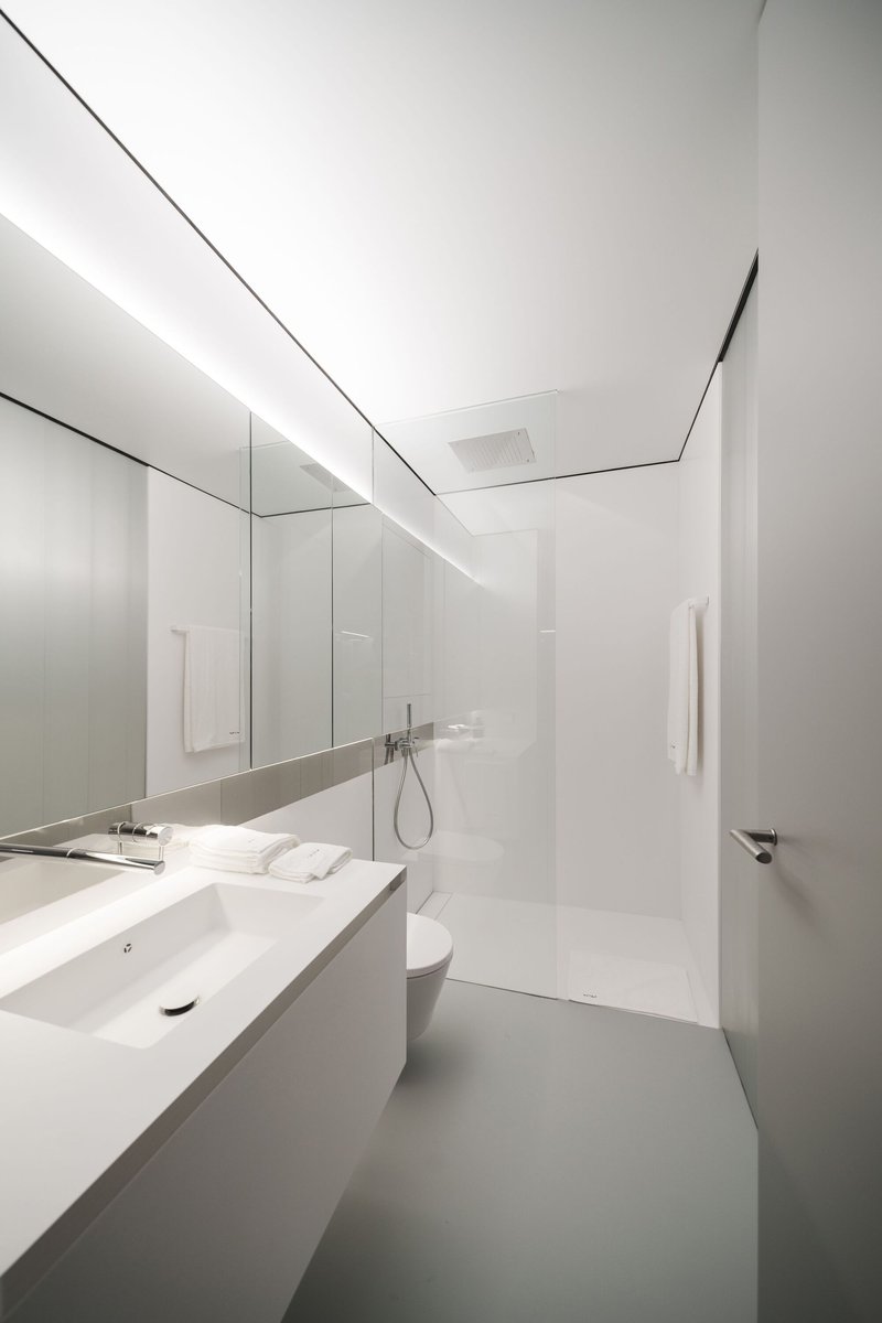 White bathroom with continuous mirror wall, floating vanity and recessed ceiling light slot