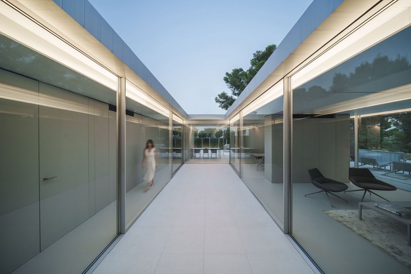 Glass corridor connecting two pavilions with a figure walking through at twilight