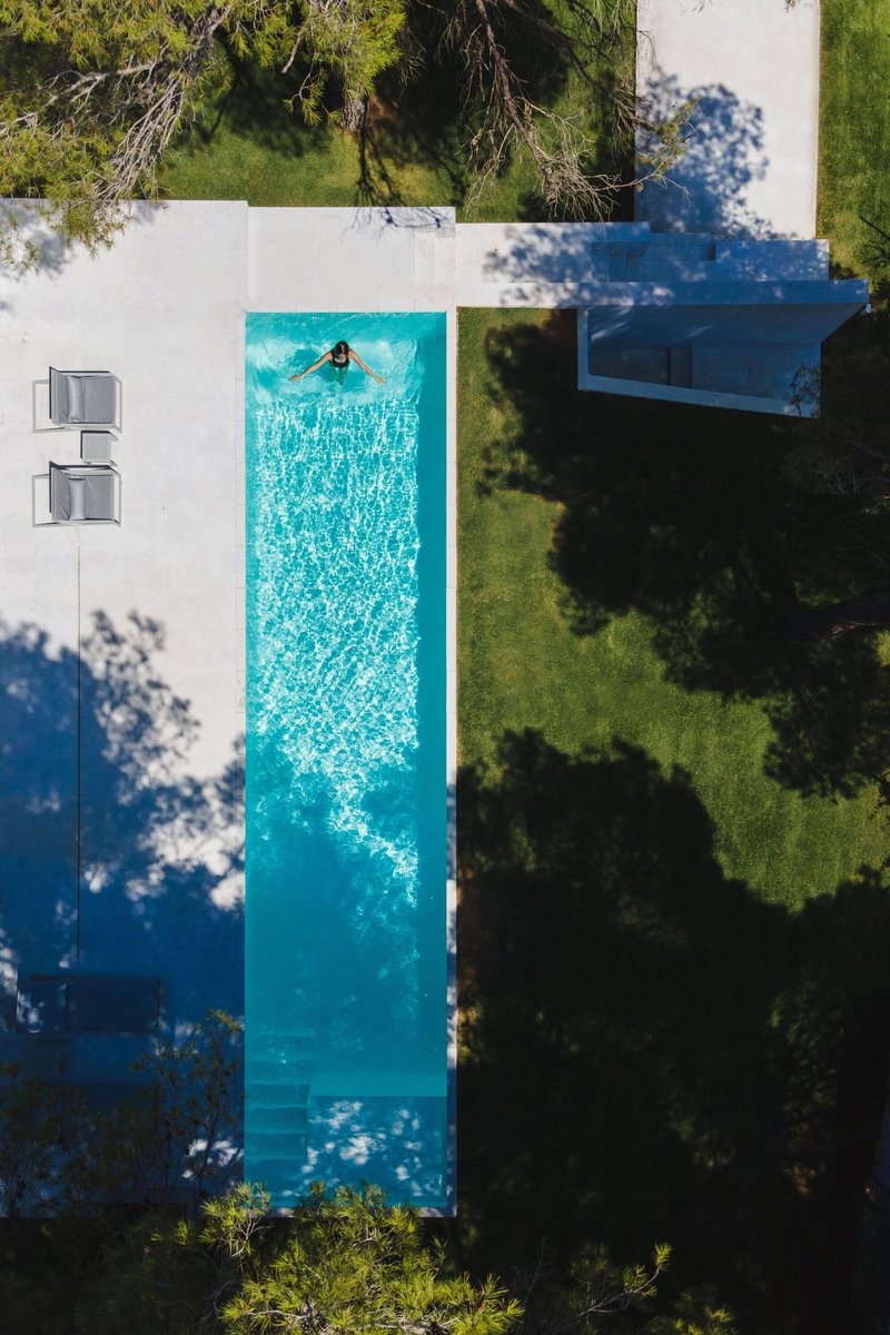 Aerial view of the lap pool with a swimmer surrounded by white paving and lawn under tree shadows