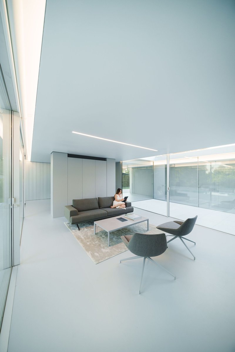 Living room with floor-to-ceiling glass walls and continuous linear ceiling slot illuminating white flooring