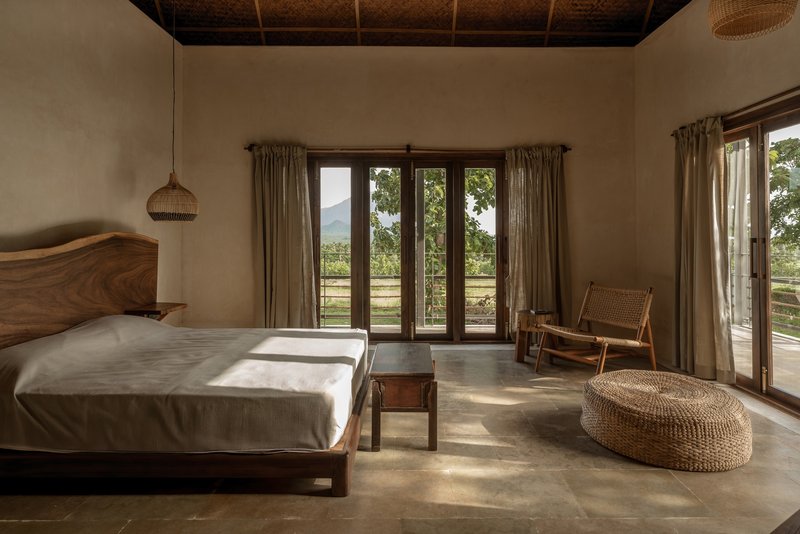 Bedroom with woven bamboo ceiling and timber-framed glazed doors opening to a mountain view