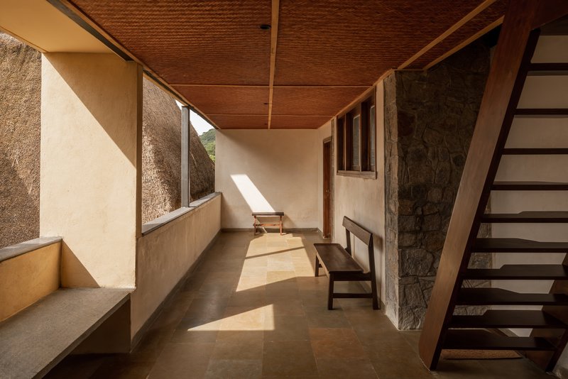 Corridor with woven bamboo ceiling, stone wall, and timber staircase bathed in afternoon sunlight